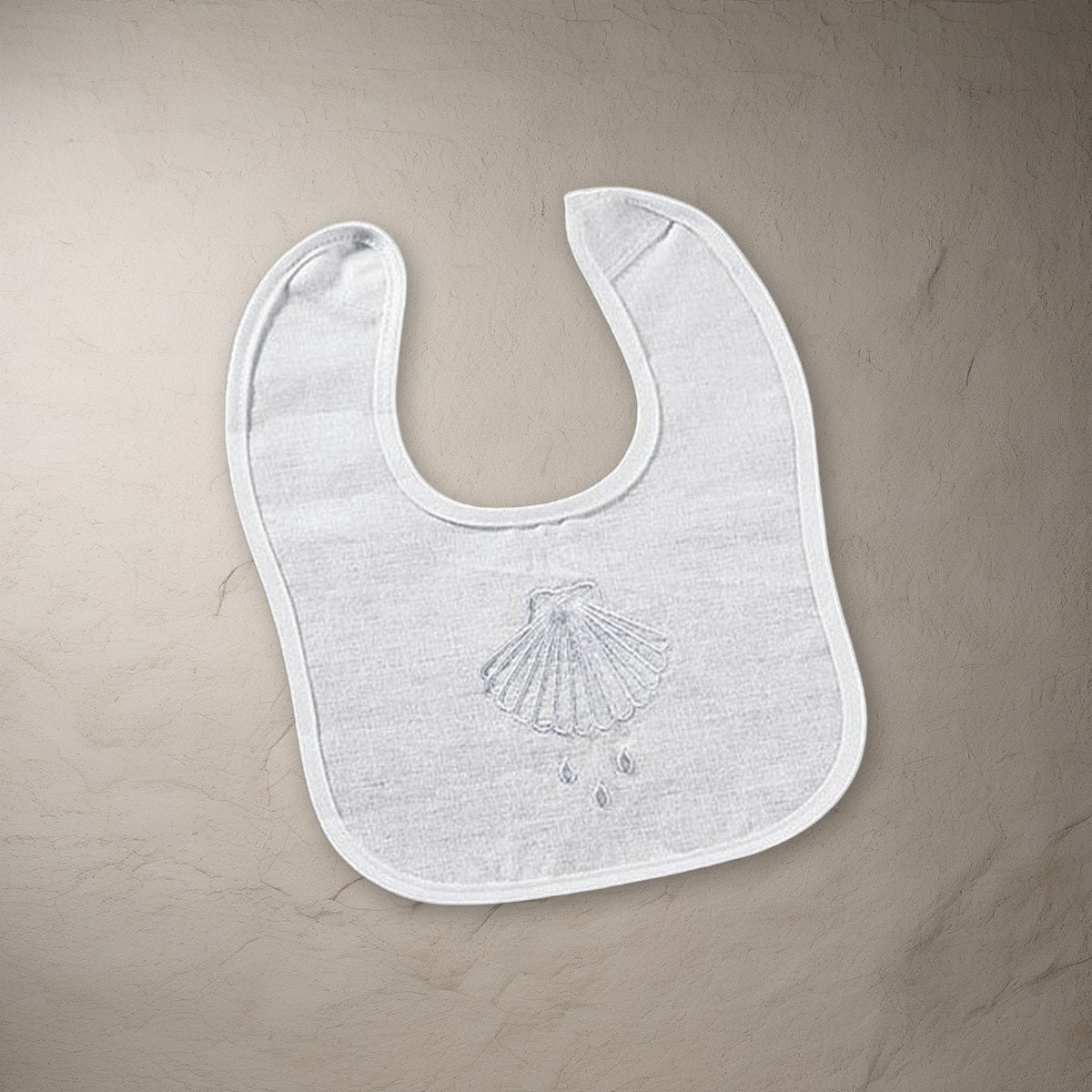 Shell & Water Embroidered Baptismal Bib 12/pk on a stone background
